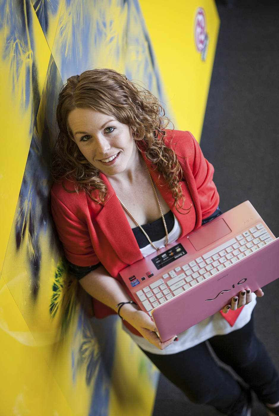 Carly Crossley holding laptop leans against wall