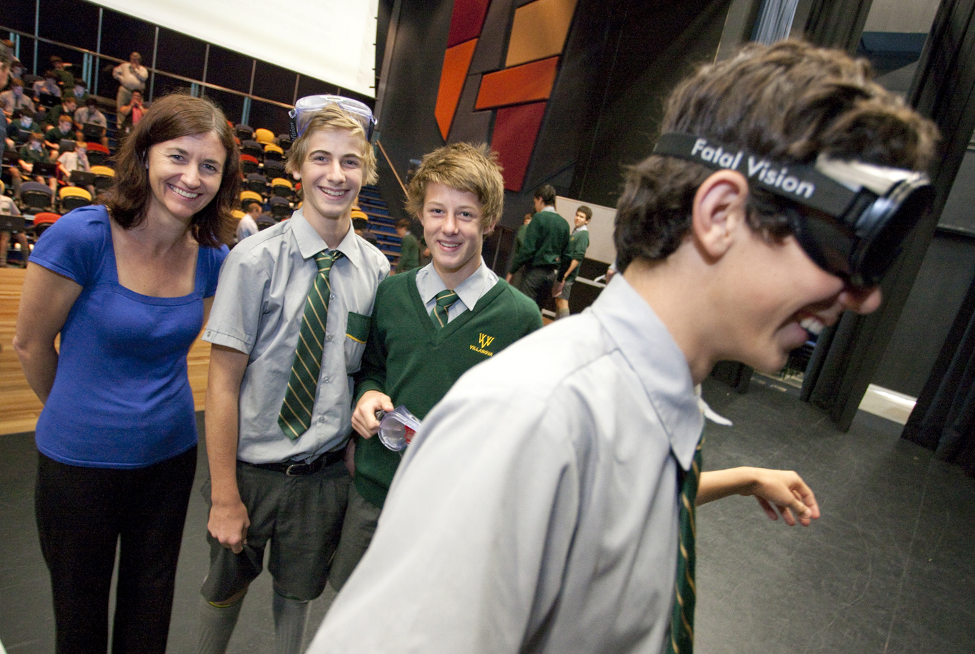 Teenage boy walks wearing goggles, watched by two teens and adult in background.