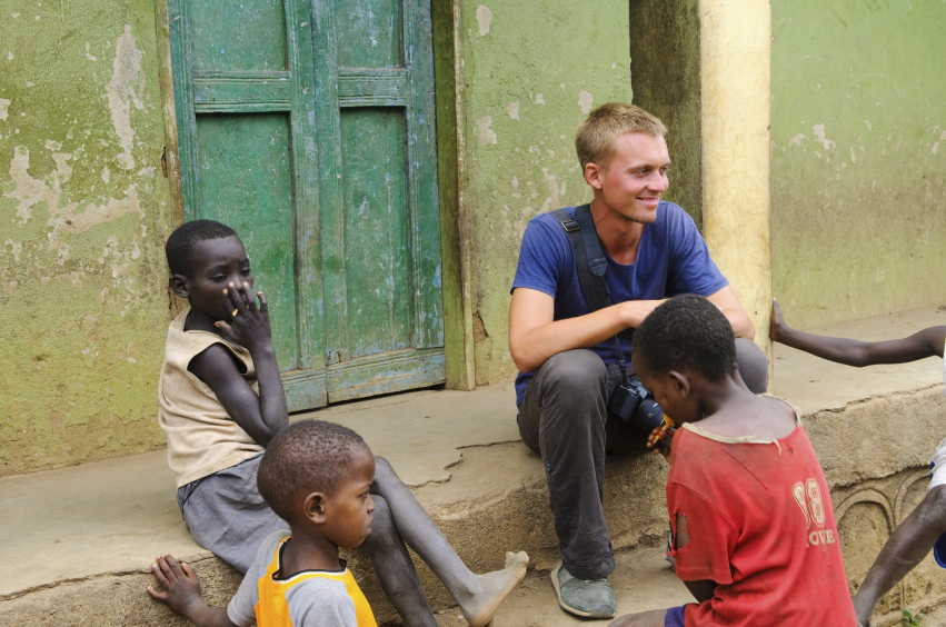 Young man sits on doorstep with three African children.
