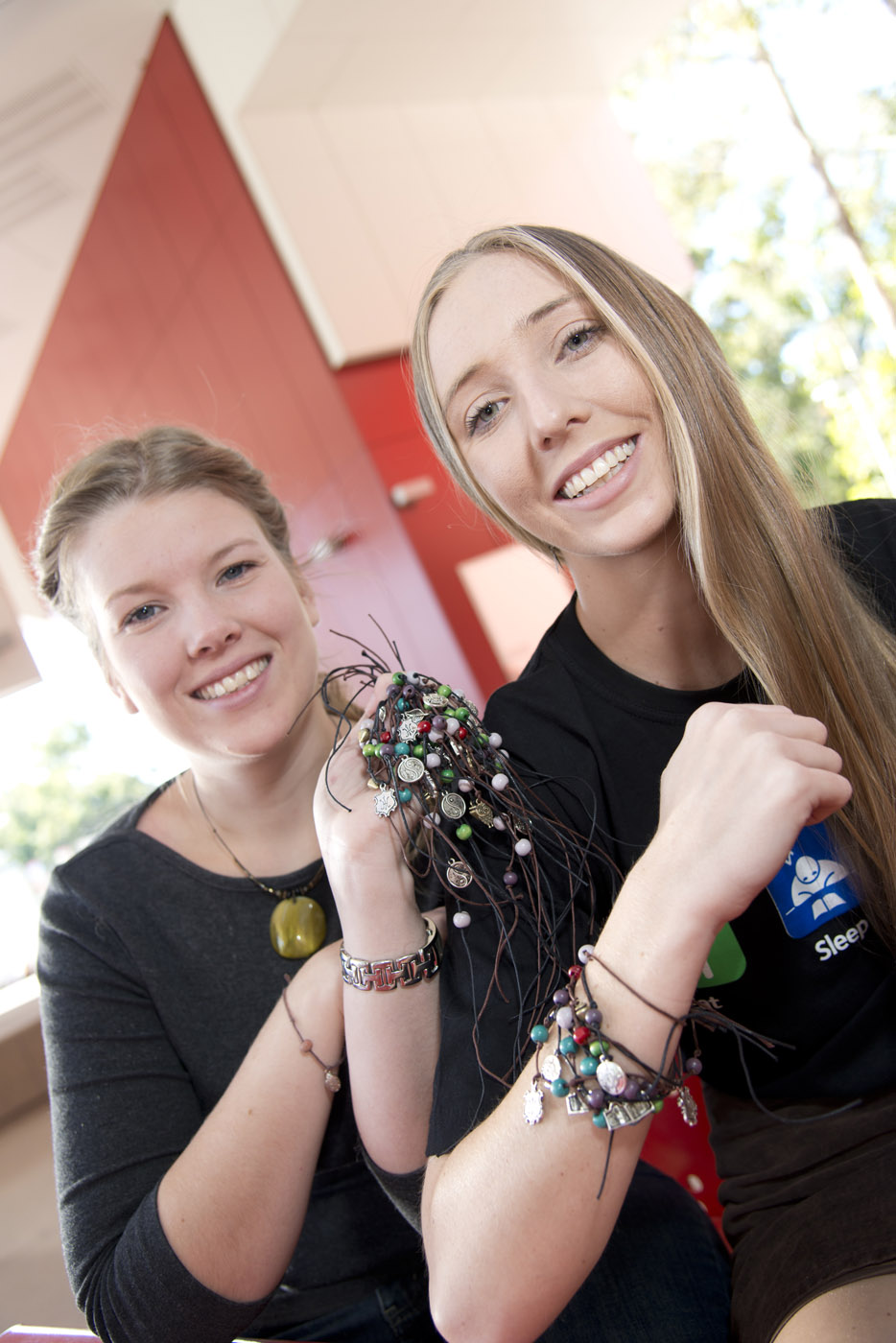 Two young ladies facing camera displaying homemade bracelents.