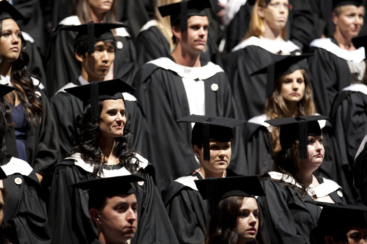 Group of graduating students at ceremony, dressed in gowns and mortar boards.