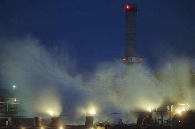 Industrial scene with large factory chimneys sending smoke into a night sky.