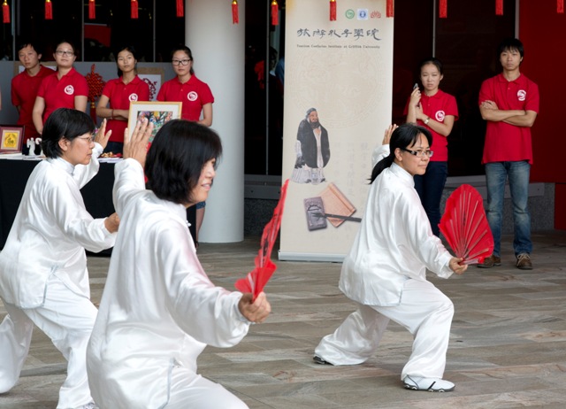 A group of performers, dressed in white, holding red fans, in action at the opening of the Tourism Confucius Insitute.
