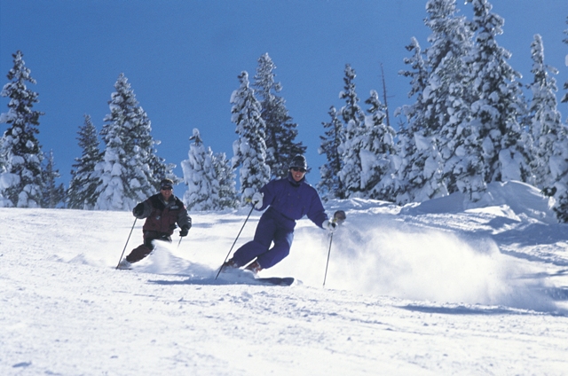 Two skiers on snow moving downhill.