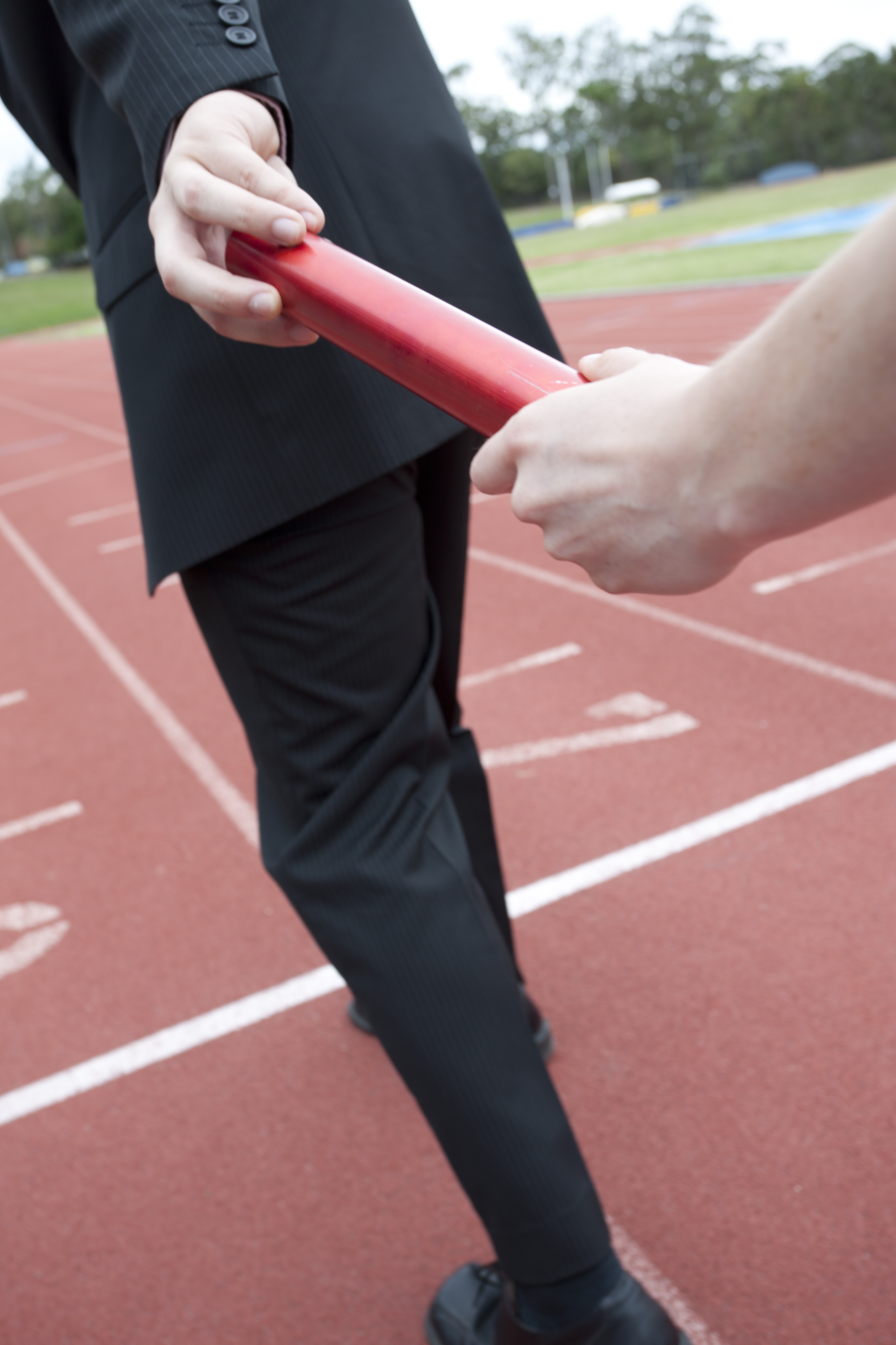 Runner passing a baton to a man in a business suit