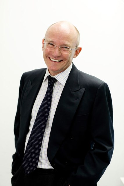 Ian Fenwick, in shirt and tie, smiling, leaning forward slightly, with hands in pockets.