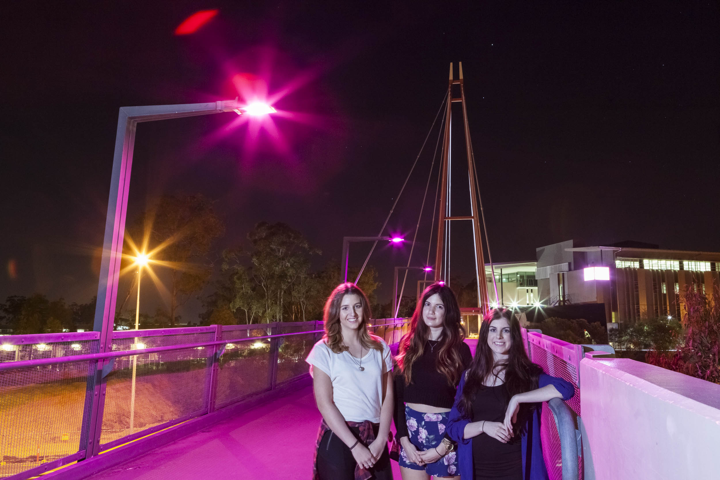Griffith students, from left, Tayela Petterwood, Bianca Serrano and Isabella Rosson take a stroll across the Smith Street bridge, lit pink for Breast Cancer Awareness Month
