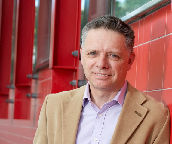 Portrait of Dr Nick Barter, Director MBA, leading on red wall