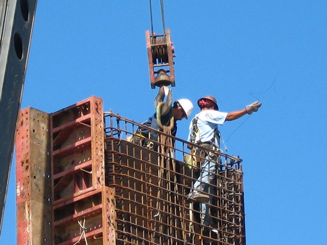 Image shows two construction workers at the top of a building site, with blue sky in background.