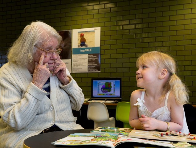 A child and older woman look at a book together in a library