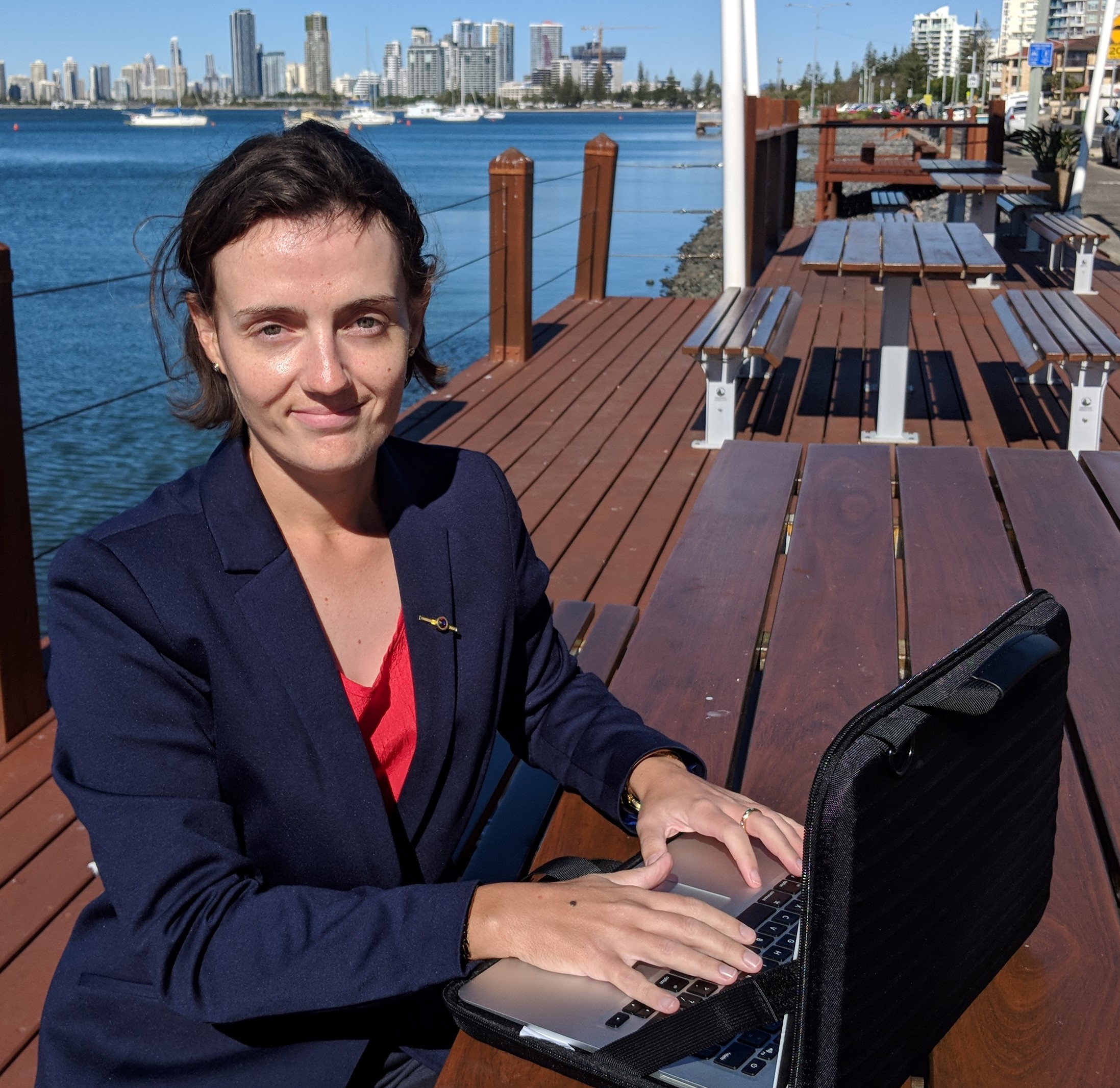 Dr Ashley Berge, seated at bench with river and Gold Coast skyline in background