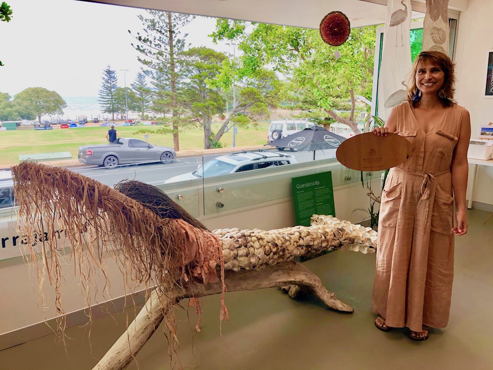 Delvene Cockatoo-Collins gains inspiration from traditional stories for her artworks, such as the shell mermaid in her new Minjerribah studio. She is holding her Griffith Business School award.