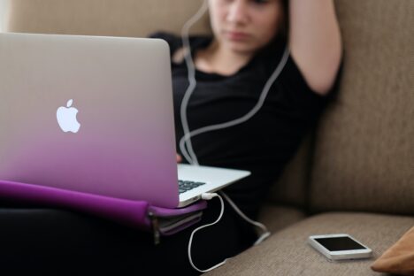 Teenage girl using a laptop with headphones and phone
