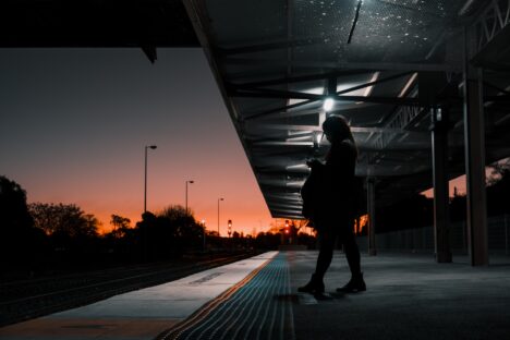 A woman stands alone at a train station at dusk