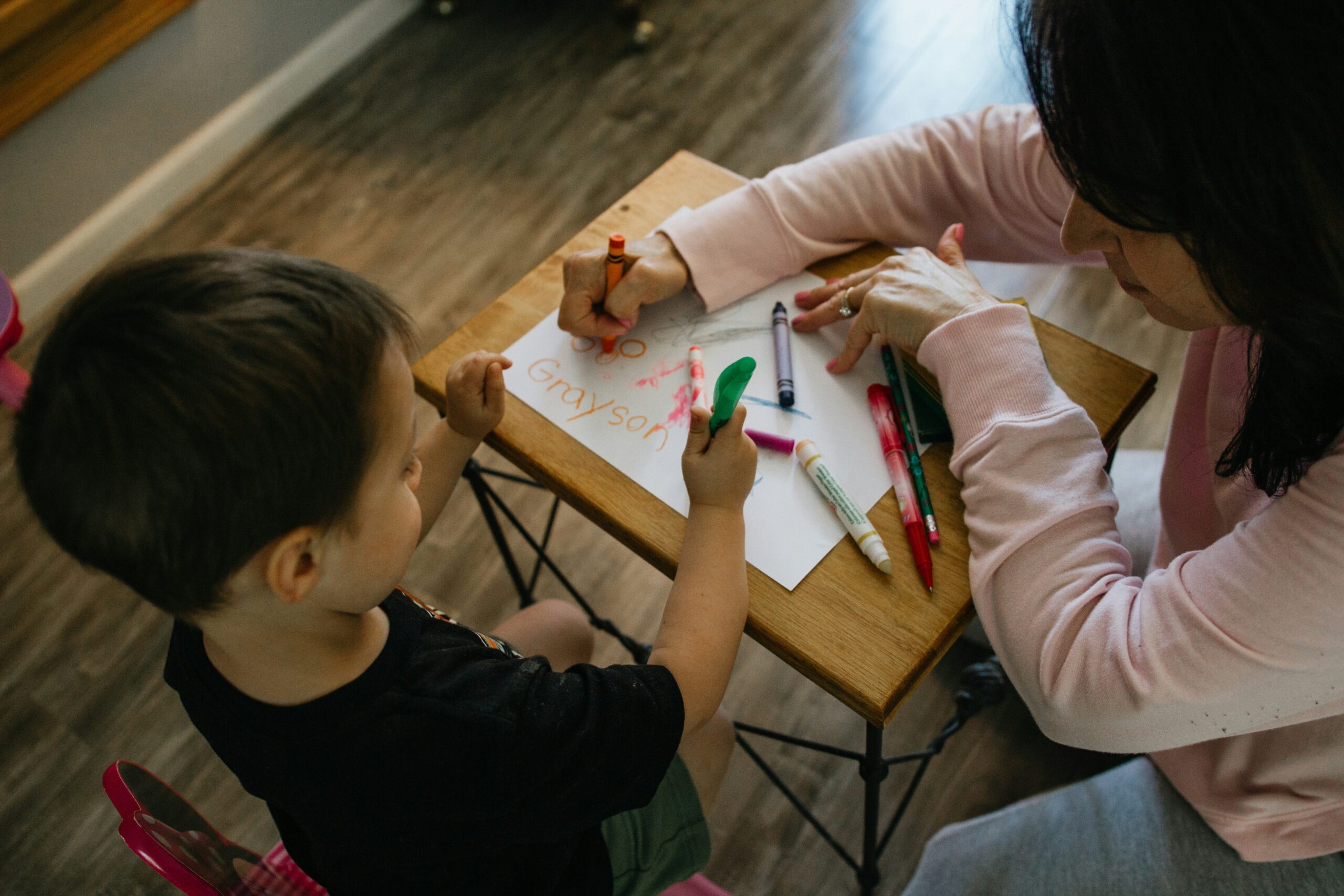 A child and adult writing with crayons