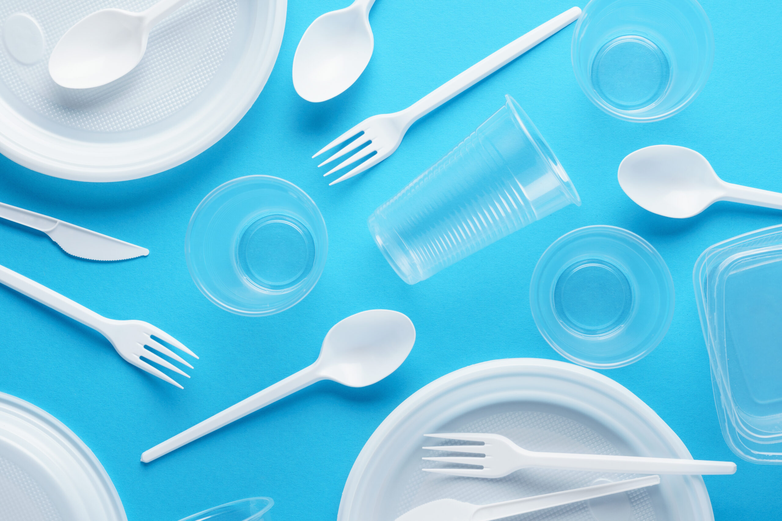 Various white plastic disposable tableware on blue background. Creative flat lay.